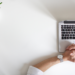A man's hands on a laptop with a plant in the background, engaged in reading business news.