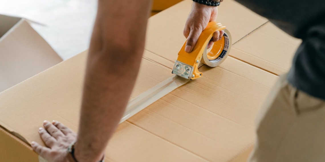 A man in a business news setting putting tape on a cardboard box.