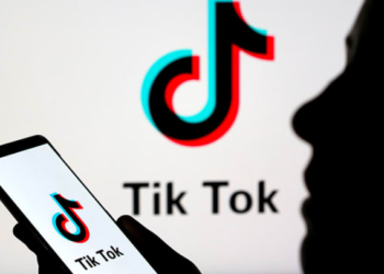 A person is holding a phone displaying the TikTok logo while reading business news.