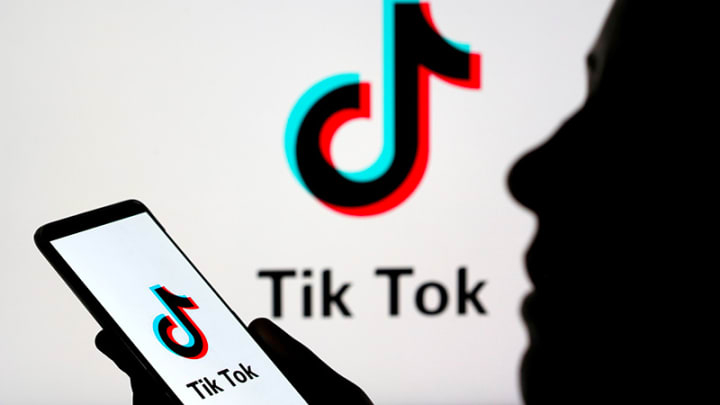 A person is holding a phone displaying the TikTok logo while reading business news.