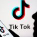 A person is holding a phone displaying the TikTok logo while reading business news.