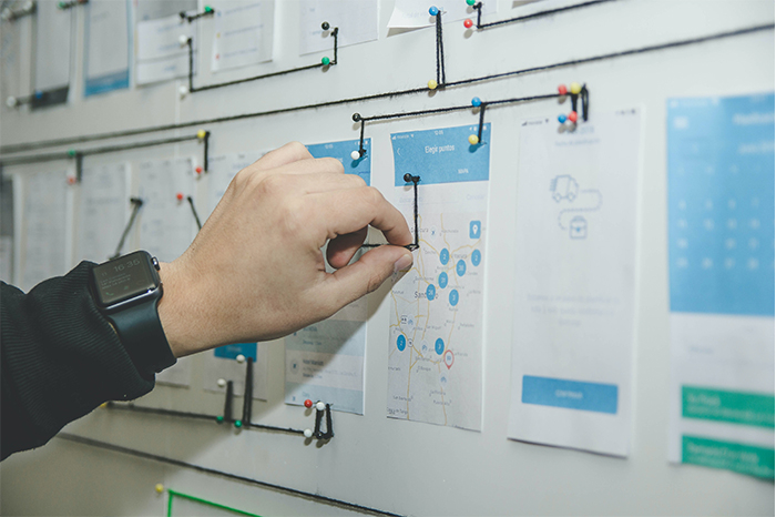 A person is pointing at a board filled with business news and a lot of paper.